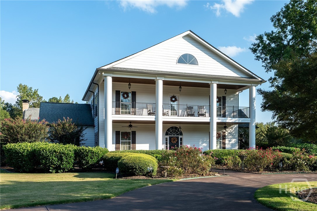 Front elevation of the main home: a white two-story Southern residence with paired columns, a stacked double veranda, and an arched gable window, above manicured boxwood gardens