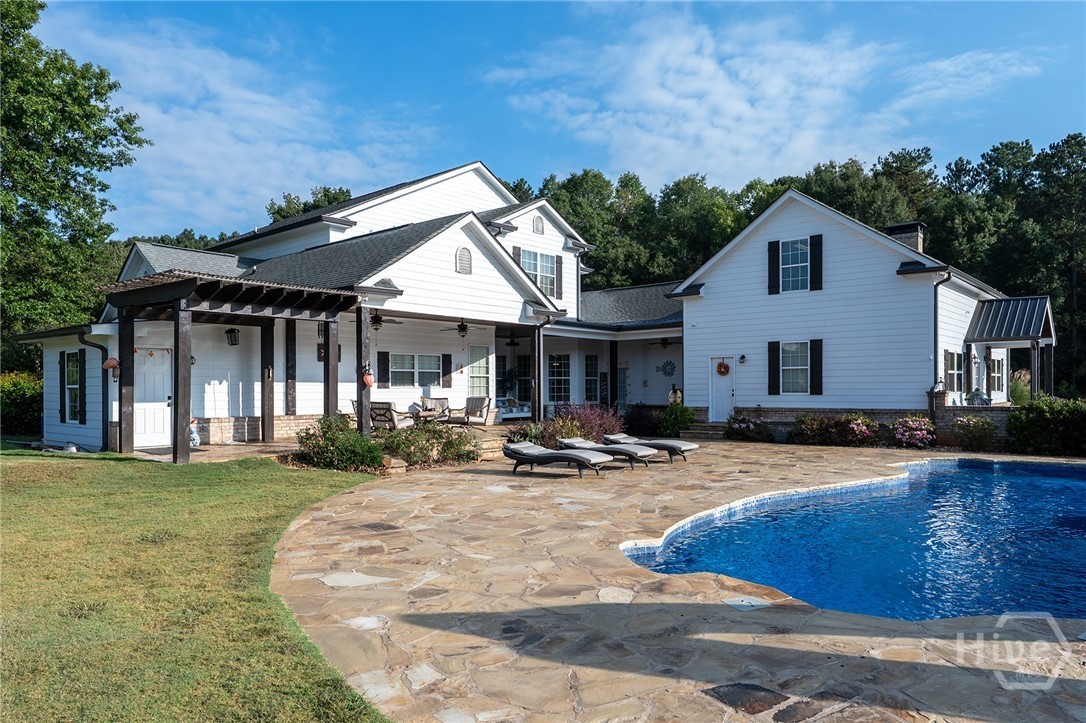 The rebuilt free-form in-ground pool behind the main home, ringed by a flagstone deck with lounge chairs and a covered patio, under a clear blue sky