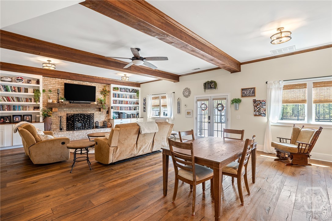 The family room with exposed stained wood ceiling beams, a brick fireplace flanked by built-in white bookcases, leather recliners, and a farm table on wide-plank hardwood floors