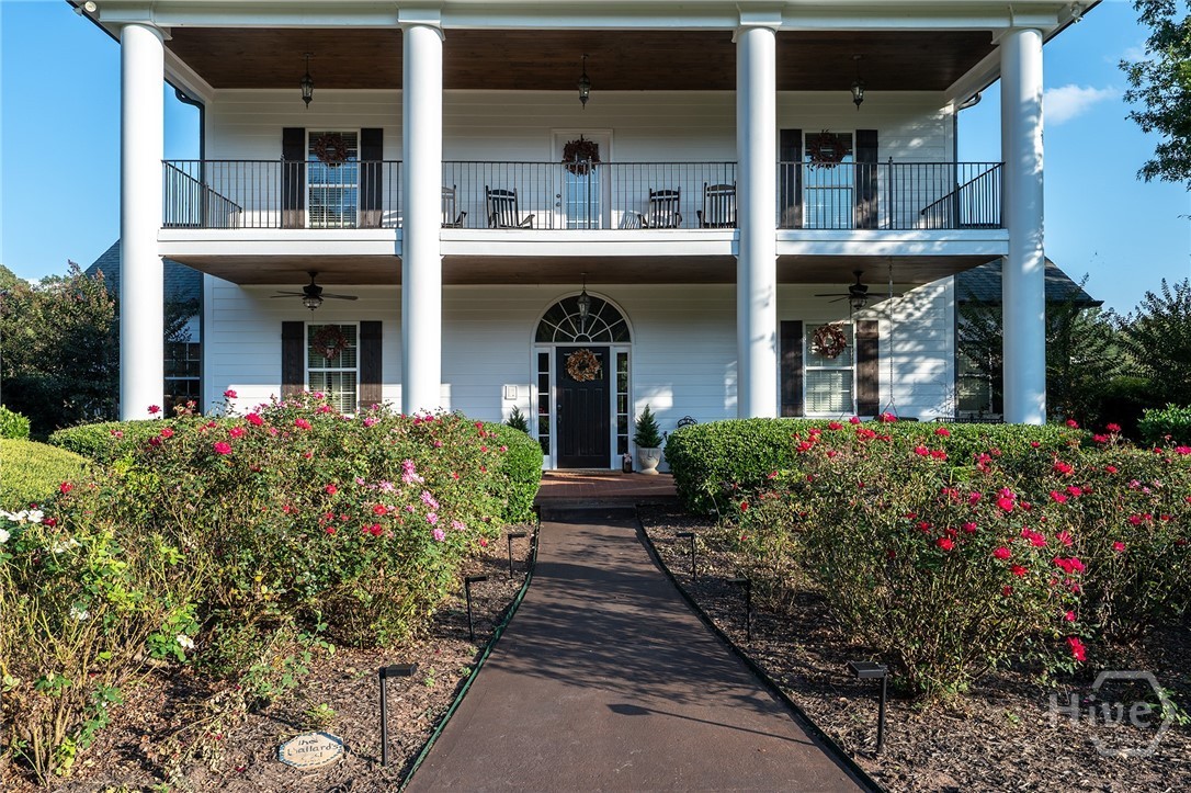 The front entry of the main home seen head-on: paired white columns framing a black front door with an arched transom, with a brick walkway leading up through a rose garden