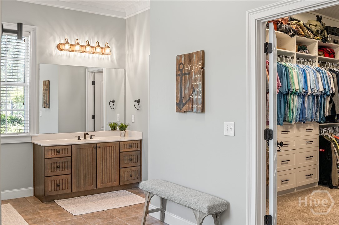 The owner's bath on the main floor with a wood double vanity beneath a row of glass globe lights, opening to a custom walk-in closet with built-in shelving and drawers