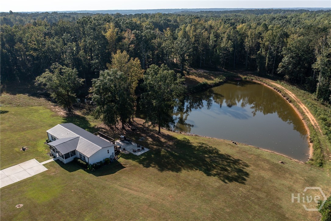 Aerial of the second home at 2202, a renovated single-story house with a metal roof and party deck, sitting on its own lawn beside a large stocked, creek-fed pond ringed by hardwood forest