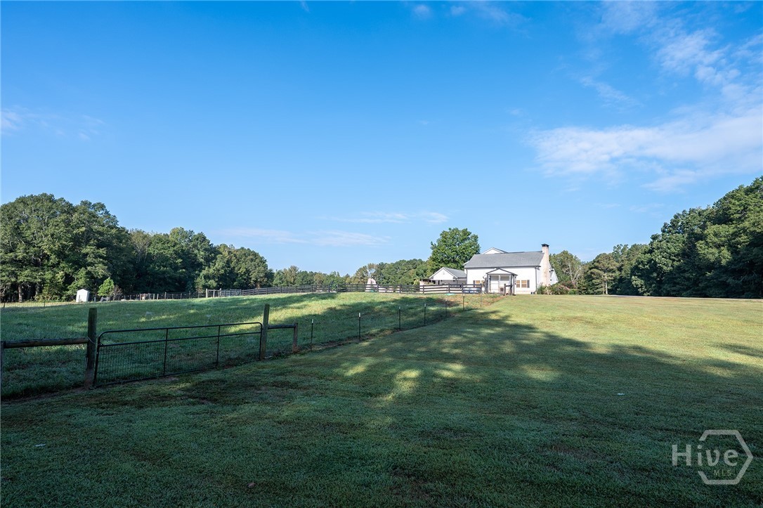 Rolling fenced and cross-fenced green pastures with wire-and-board horse fencing in the foreground, the white main home visible in the distance against a wall of hardwood forest
