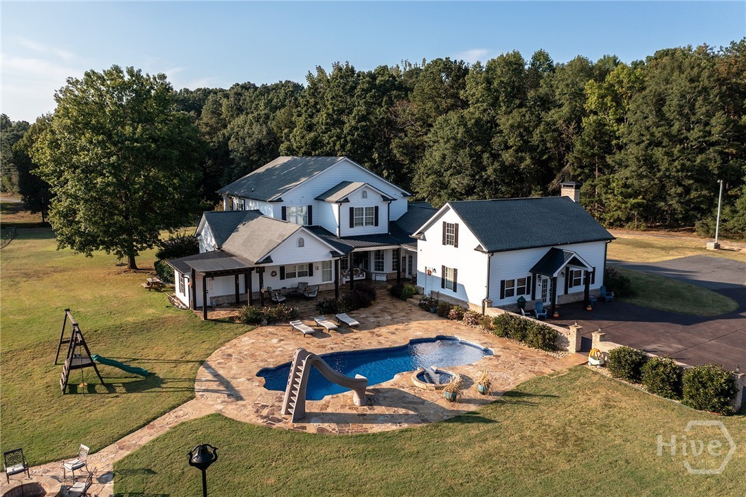 Aerial of the Ballard Estate at 2202/2206 Lem Edwards Rd, Colbert, showing the white two-story main home, a free-form resort pool with rock slide, flagstone deck, and surrounding green pastures and forest